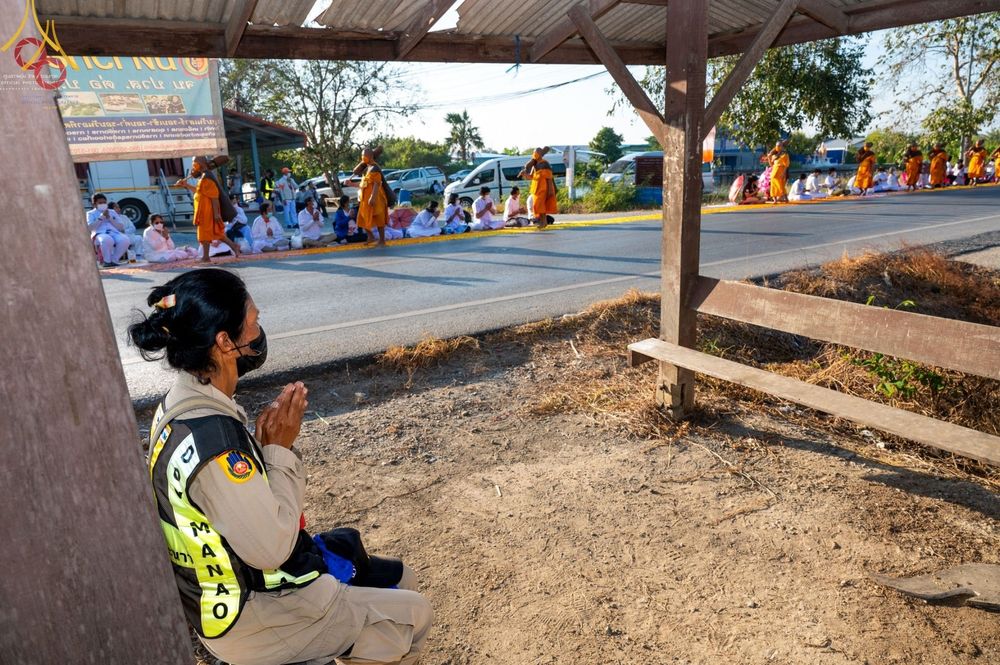 เจ้าหน้าที่และพุทธศาสนิกชนนั่งพนมมือรอต้อนรับคณะพระธรรมยาตราที่เดินธุดงค์ผ่านบริเวณริมถนนหน้าวัดบางปลา