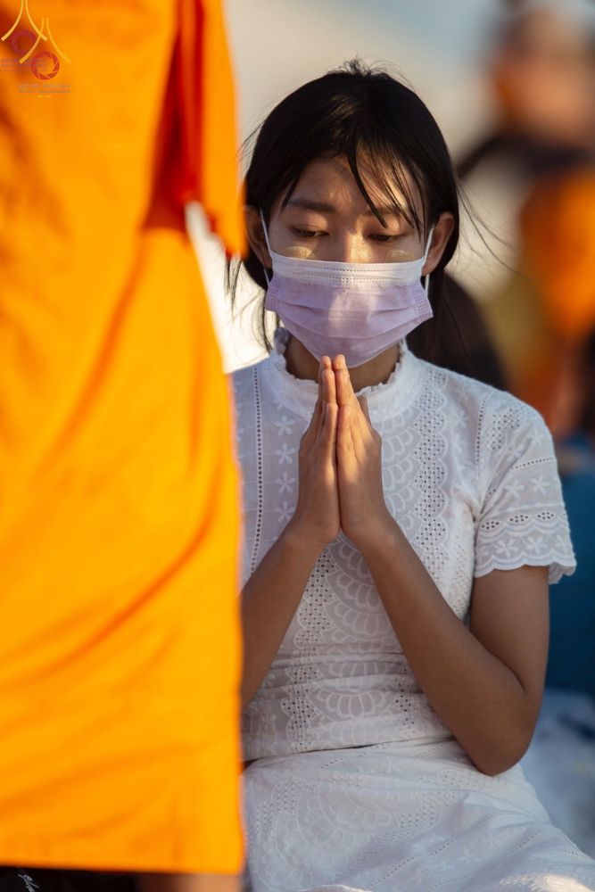 หญิงสาวสวมชุดขาวพนมมือต้อนรับพระธรรมยาตราในพิธีทางศาสนา