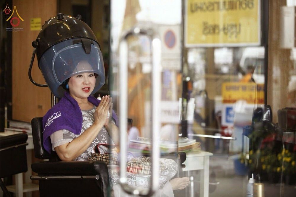หญิงไทยนั่งอบผมในร้านทำผมพนมมือต้อนรับคณะพระธุดงค์ที่เดินผ่านหน้าร้าน