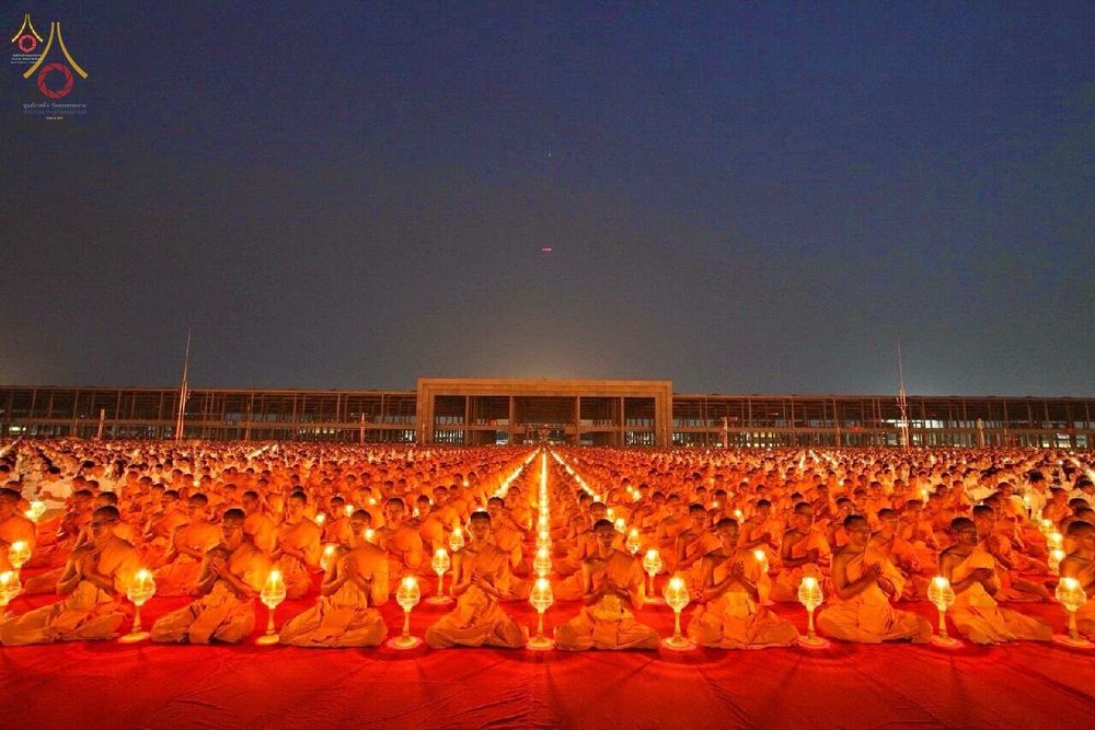 พระภิกษุสงฆ์จำนวนมากนั่งเรียงแถวถือโคมประทีปสว่างไสวในพิธีทางศาสนาช่วงค่ำคืน