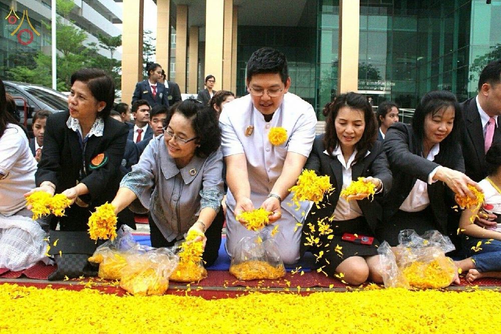 กลุ่มพุทธศาสนิกชนกำลังโปรยกลีบดอกดาวเรืองสีเหลืองลงบนพื้นเพื่อต้อนรับพระธุดงค์