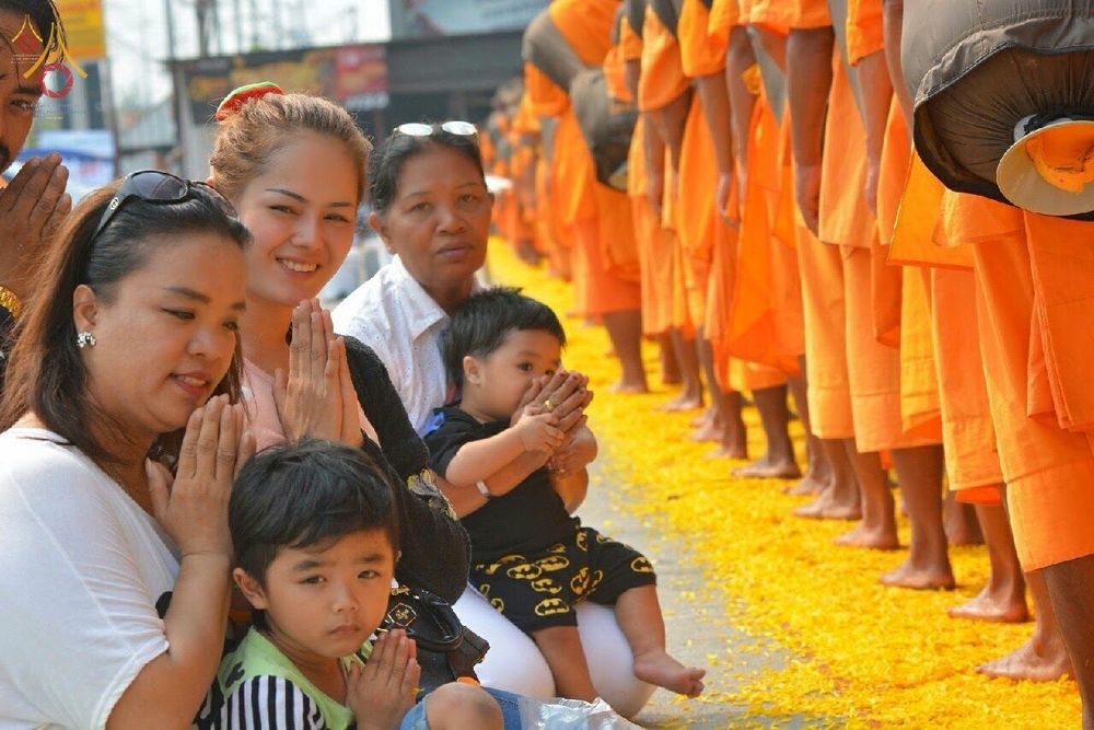 กลุ่มพุทธศาสนิกชนนั่งพนมมือต้อนรับคณะพระธุดงค์ที่เดินผ่านเส้นทางโปรยดอกดาวเรือง