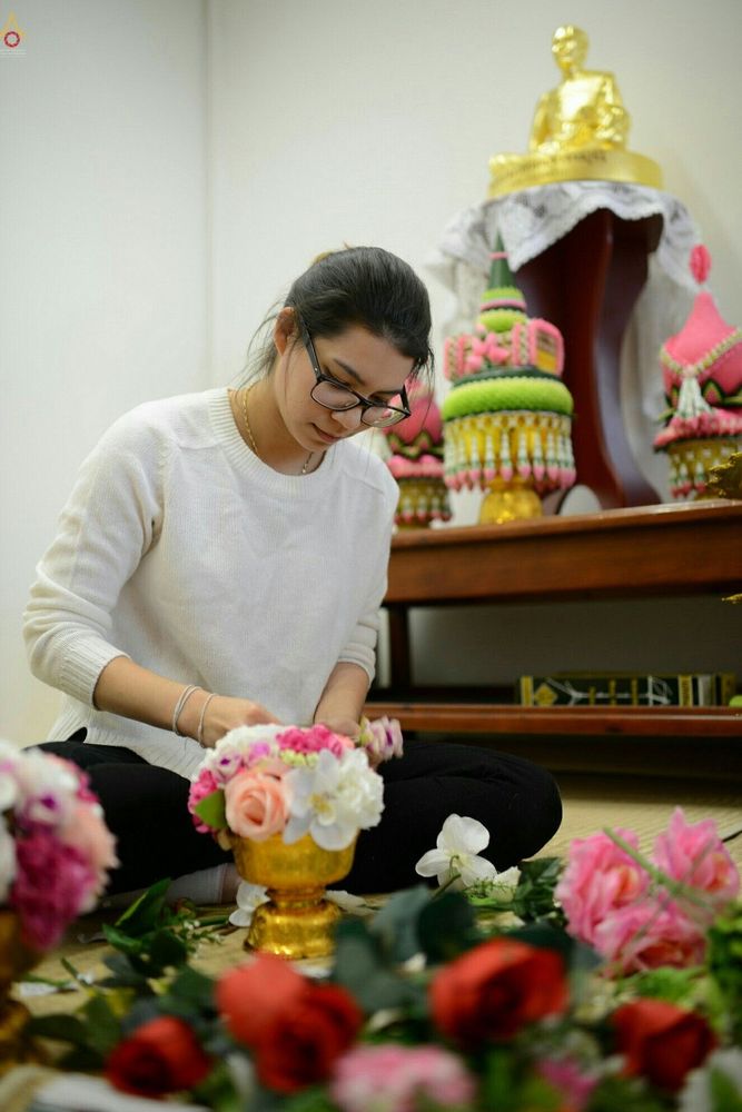 หญิงสาวสวมแว่นตากำลังจัดพานดอกไม้สดเพื่อเตรียมใช้ในพิธีทางศาสนาภายในวัดพุทธไอซ์แลนด์