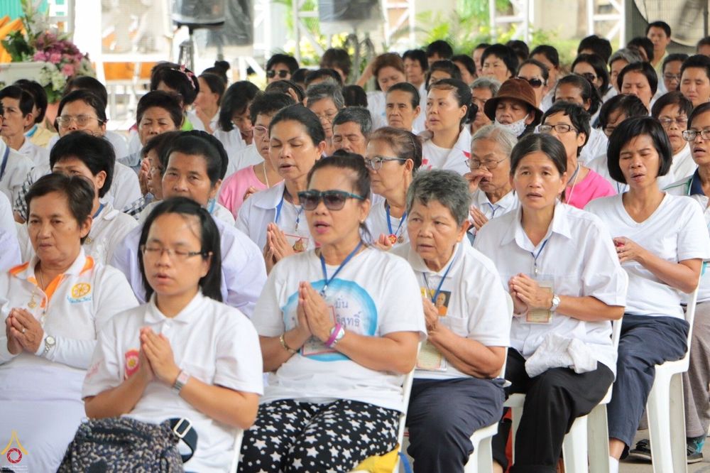 กลุ่มพุทธศาสนิกชนสวมชุดขาวนั่งพนมมือร่วมพิธีเจริญชัยมงคลคาถาถวายพระพรและย่ำกลองระฆัง ณ วัดพระธรรมกาย