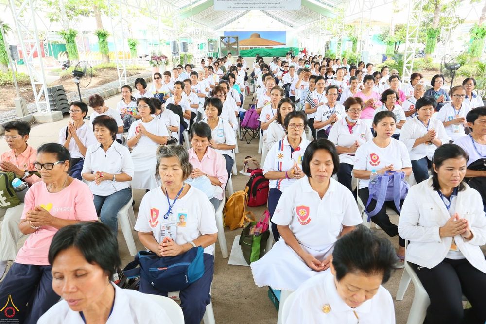 พุทธศาสนิกชนสวมชุดขาวนั่งพนมมือร่วมพิธีเจริญชัยมงคลคาถาถวายพระพรและย่ำกลองระฆัง ณ วัดพระธรรมกาย