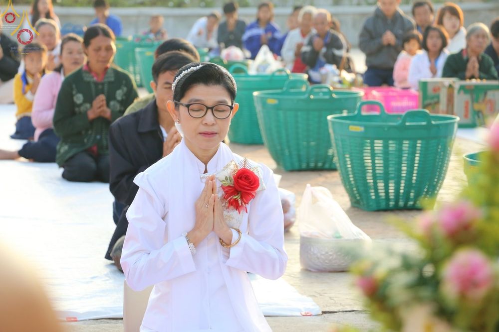 หญิงไทยสวมชุดขาวพนมมือไหว้ในพิธีตักบาตรข้าวสารอาหารแห้งที่วัดกิ่วลม
