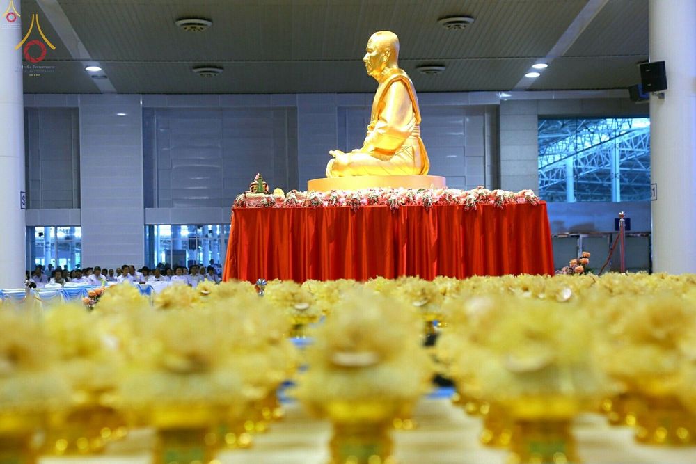 รูปหล่อทองคำพระมงคลเทพมุนีประดิษฐานบนแท่นที่มีผ้าคลุมสีแดงและพานพุ่มดอกไม้สีทองวางเรียงรายในอาคาร