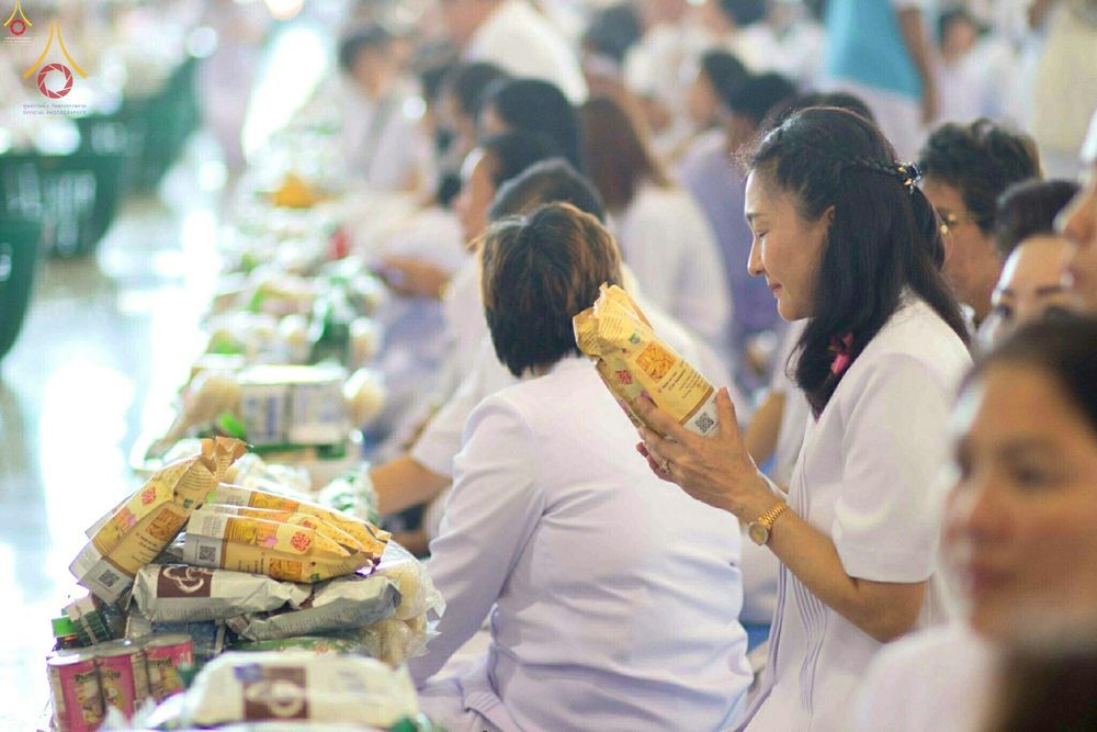 พุทธศาสนิกชนสวมชุดขาวกำลังจัดเตรียมเครื่องไทยธรรมและอาหารแห้งเพื่อนำไปถวายพระสงฆ์ในงานบุญ