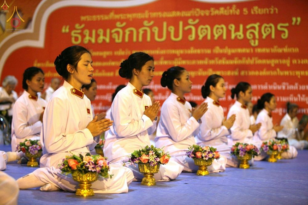 กลุ่มอุบาสิกาชุดขาวนั่งพนมมือปฏิบัติธรรมหน้าป้ายธรรมจักกัปปวัตตนสูตร