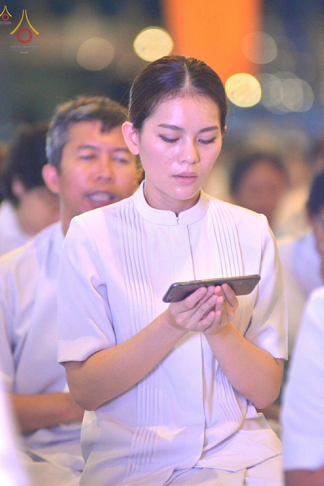 หญิงสาวสวมชุดสีขาวถือโทรศัพท์มือถือด้วยความตั้งใจในงานพิธีกรรมทางศาสนา