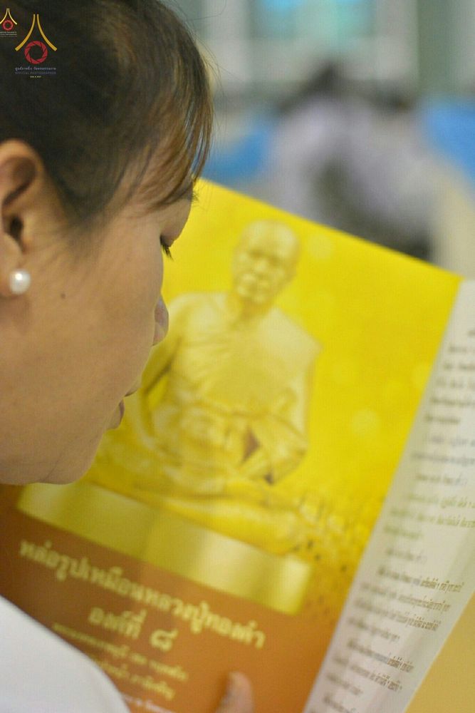 หญิงสาวสวมชุดขาวกำลังอ่านหนังสือที่มีรูปเหมือนหลวงปู่สีทองบนหน้าปกอย่างตั้งใจ