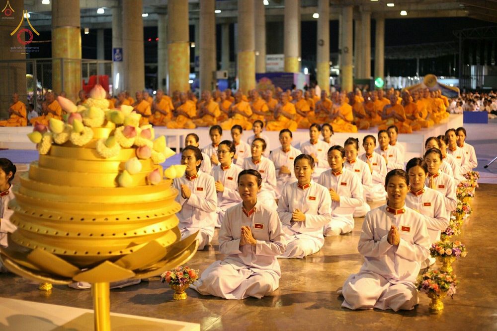 พุทธศาสนิกชนในชุดขาวนั่งพนมมือปฏิบัติธรรมในพิธีวันครูผู้ค้นพบวิชชาธรรมกาย โดยมีพระภิกษุสงฆ์นั่งอยู่ด้านหลัง