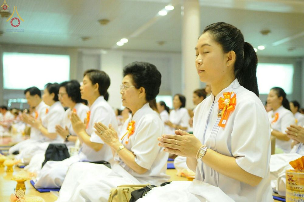 กลุ่มพุทธศาสนิกชนสวมชุดขาวนั่งสมาธิและพนมมือด้วยความสงบภายในอาคาร เพื่อร่วมกิจกรรมเนื่องในวันครูผู้ค้นพบวิชชาธรรมกาย