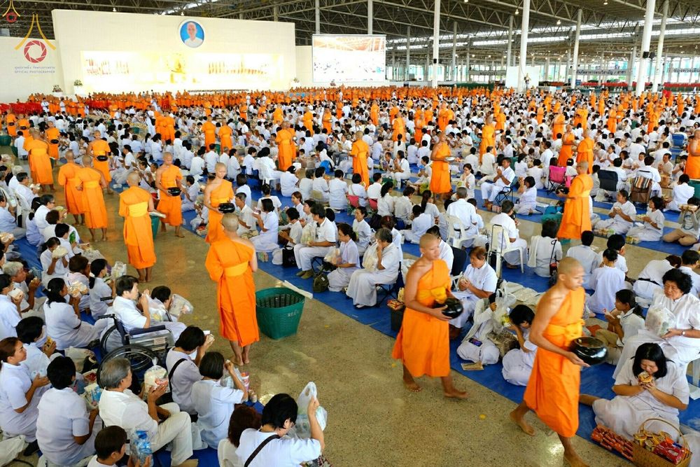 พระภิกษุสงฆ์และพุทธศาสนิกชนชุดขาวจำนวนมากร่วมกิจกรรมตักบาตรภายในอาคารขนาดใหญ่ในวันครูผู้ค้นพบวิชชาธรรมกาย