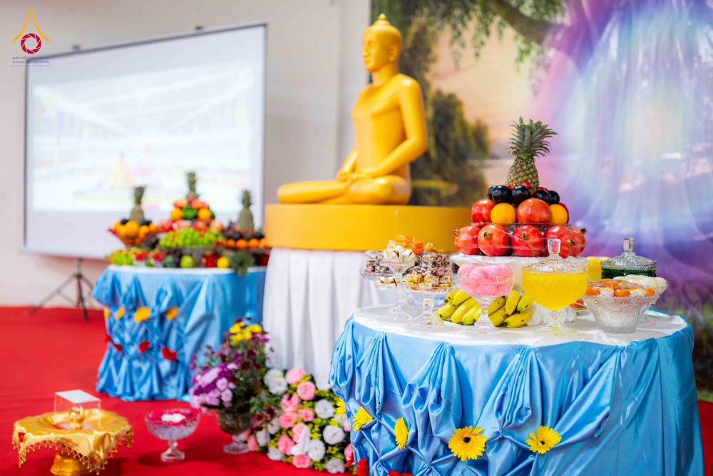 โต๊ะวางเครื่องบูชาที่มีผลไม้และขนมหวานจัดวางอยู่หน้าพระพุทธรูปสีทองในห้องโถง