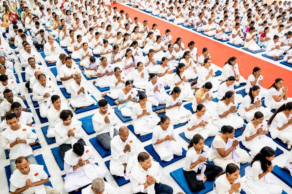 กลุ่มคนสวมชุดสีขาวนั่งพนมมือปฏิบัติธรรมจำนวนมากภายในอาคาร