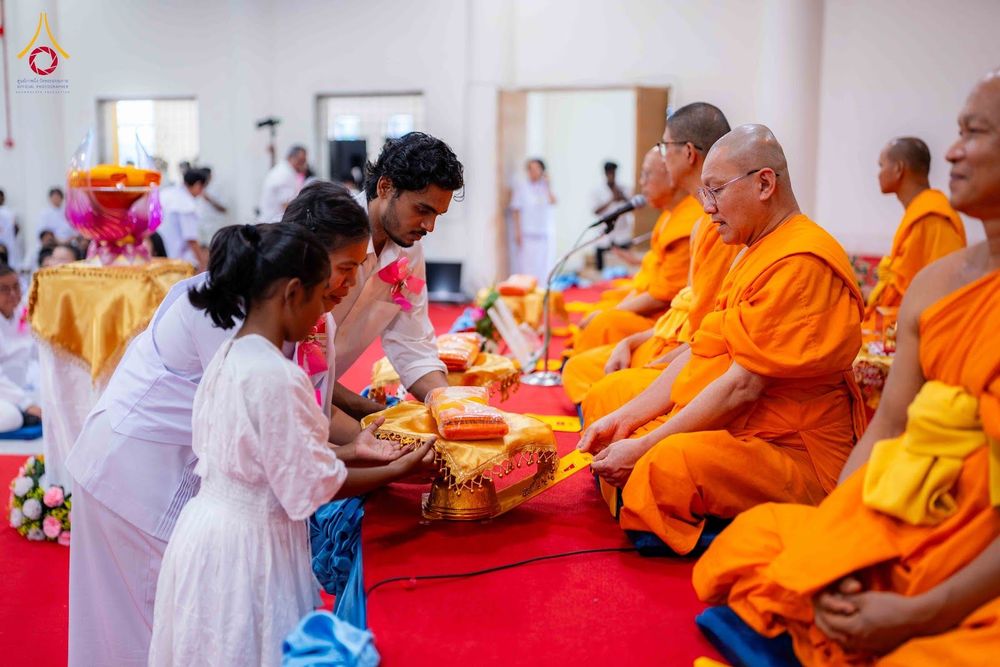 ผู้เข้าร่วมโครงการในชุดสีขาวกำลังถวายผ้าไตรแด่พระภิกษุสงฆ์ในพิธีทางศาสนา