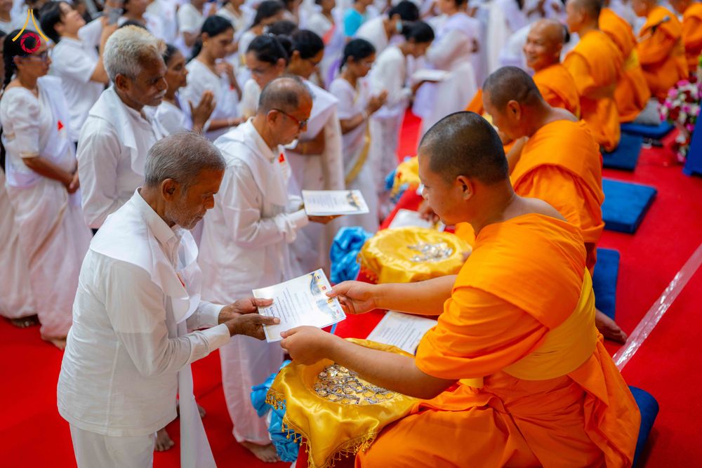 พระภิกษุกำลังส่งมอบวุฒิบัตรให้แก่ผู้เข้าร่วมโครงการอบรมในชุดสีขาวภายในวัด