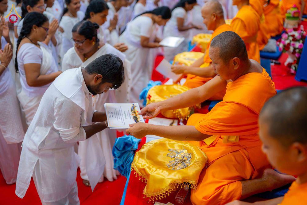 พระภิกษุกำลังส่งมอบเอกสารวุฒิบัตรให้แก่ชายในชุดสีขาวท่ามกลางผู้เข้าร่วมพิธีในชุดสีขาว