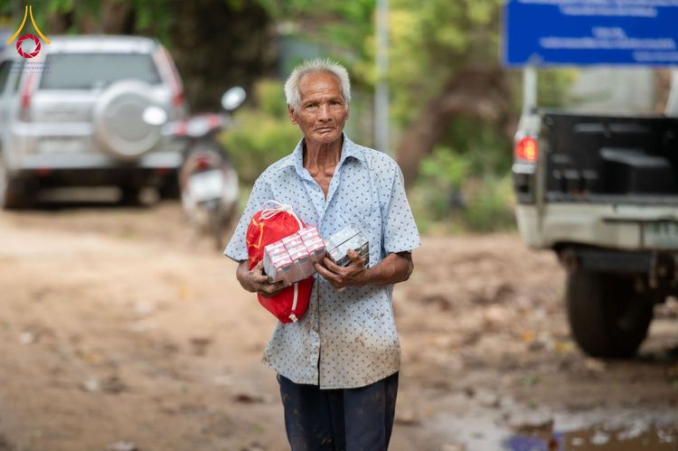 ชายสูงวัยถือถุงและกล่องสิ่งของบรรเทาทุกข์ในพื้นที่กลางแจ้ง
