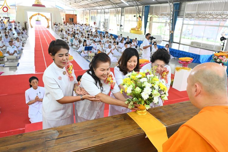 กลุ่มสุภาพสตรีในชุดสีขาวกำลังถวายพานดอกไม้แด่พระภิกษุสงฆ์ในพิธีทางศาสนา