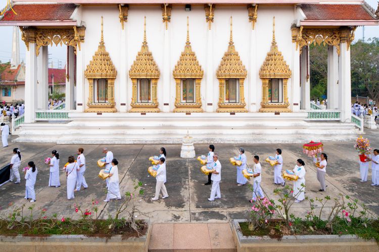 กลุ่มคนชุดขาวเดินถือพานพุ่มและเครื่องไทยธรรมหน้าพระอุโบสถวัด