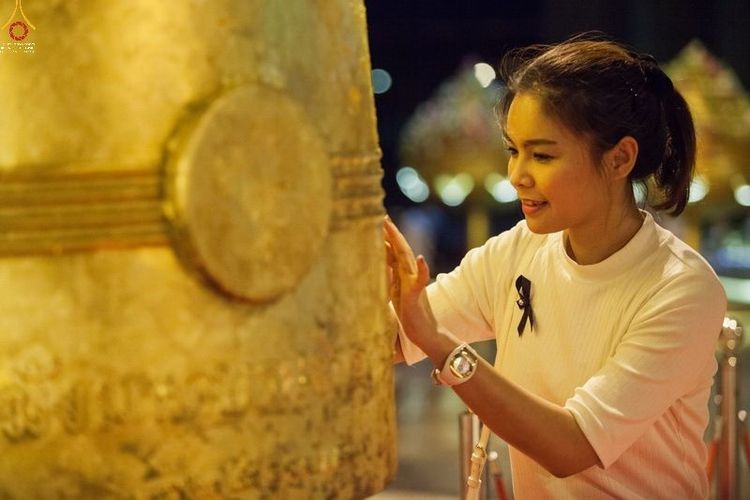 หญิงสาวกำลังใช้มือปิดแผ่นทองลงบนระฆังใบใหญ่ในพิธีทางศาสนา