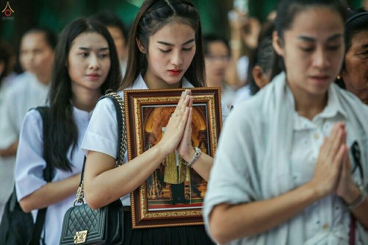 หญิงสาวถือกรอบรูปพระบรมฉายาลักษณ์พนมมือด้วยความสำรวมในพิธีบรรพชาอุปสมบท