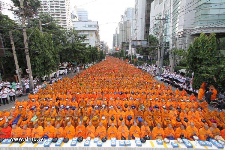 พระภิกษุสงฆ์จำนวนมากนั่งเรียงแถวรับบิณฑบาตบนถนนในเมือง