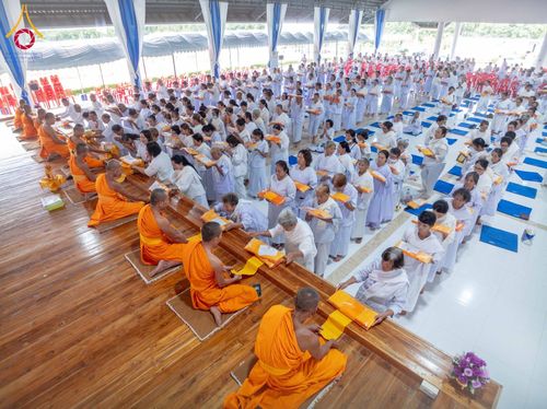 พุทธศาสนิกชนชุดขาวเข้าแถวถวายสังฆทานแด่พระภิกษุสงฆ์ในอาคารปฏิบัติธรรม