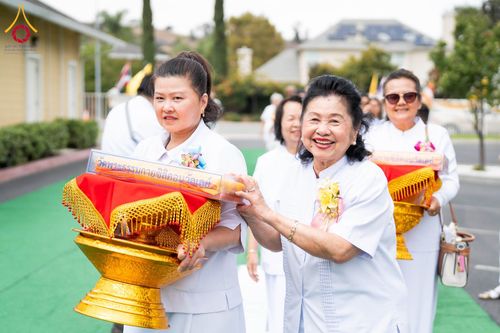 กลุ่มผู้หญิงสวมชุดขาวถือพานพุ่มสีทองในขบวนพิธีทอดผ้าป่า
