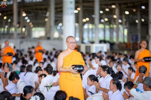พระภิกษุถือบาตรเดินในพิธีตักบาตรท่ามกลางพุทธศาสนิกชนชุดขาว