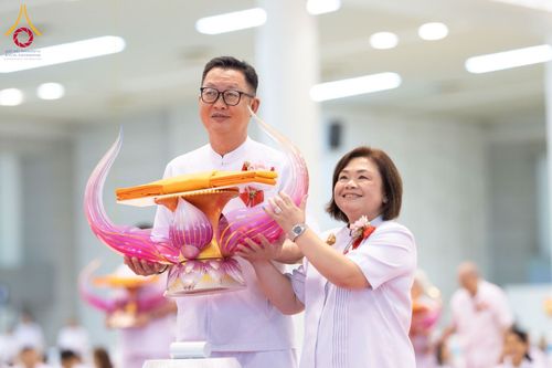 ชายและหญิงสวมชุดสีขาวถือพานพุ่มผ้าไตรจีวรในพิธีทางศาสนา