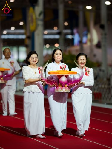 กลุ่มพุทธศาสนิกชนสวมชุดขาวถือพานพุ่มผ้าไตรเดินบนพรมแดงในพิธีทางศาสนา