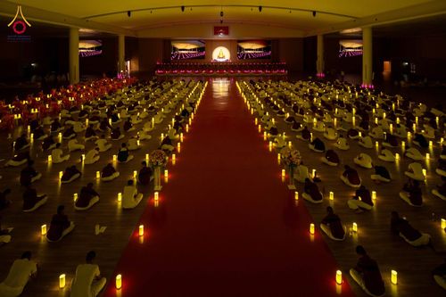 ผู้คนจำนวนมากนั่งปฏิบัติธรรมและจุดเทียนรวมใจภายในห้องโถงกว้างที่มีทางเดินสีแดงตรงกลาง