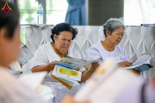 ผู้หญิงสูงอายุสวมชุดสีขาวกำลังอ่านหนังสือในกิจกรรมอบรม