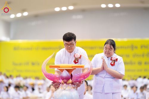 ชายและหญิงสวมชุดสีขาวกำลังประคองพานผ้าไตรจีวรในพิธีทางศาสนา