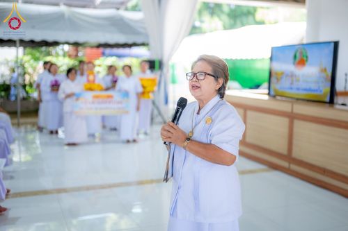 สุภาพสตรีสวมชุดขาวถือไมโครโฟนกำลังพูดในงานอบรมโดยมีกลุ่มคนชุดขาวอยู่ด้านหลัง