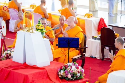 พระภิกษุสงฆ์ในจีวรสีเหลืองทองกำลังประกอบพิธีทางศาสนาพร้อมพานพุ่มและเครื่องบูชาบนโต๊ะหมู่บูชา