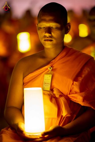 พระภิกษุถือโคมไฟส่องสว่างขณะนั่งสมาธิในพิธีจุดเทียน