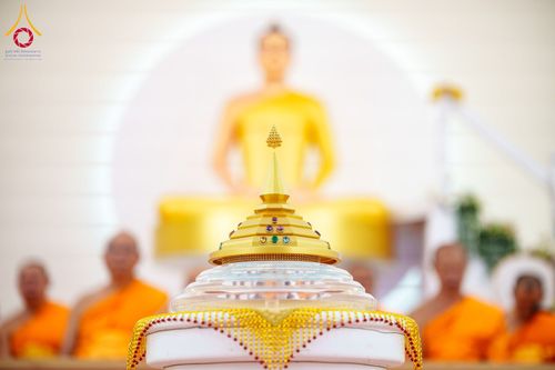 ผอบสีทองทรงเจดีย์วางอยู่หน้าพระพุทธรูปและพระภิกษุสงฆ์ในพิธีทางศาสนา