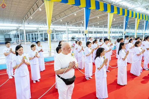 กลุ่มคนสวมชุดขาวถือสายสิญจน์พนมมือประกอบพิธีกรรมทางศาสนาภายในอาคาร