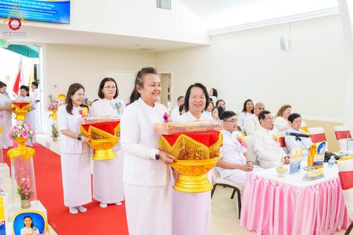 กลุ่มสาธุชนชุดขาวถือพานพุ่มผ้าป่าเดินในแถวภายในอาคารเพื่อร่วมพิธีทางศาสนา