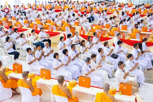 พุทธศาสนิกชนจำนวนมากในชุดสีขาวและพระภิกษุสงฆ์ร่วมพิธีทางศาสนาภายในอาคารขนาดใหญ่