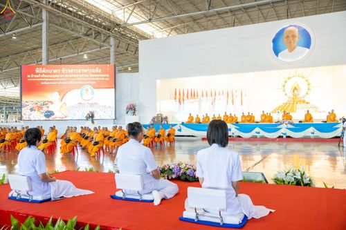 พุทธศาสนิกชนในชุดขาวนั่งร่วมพิธีตักบาตรข้าวสารอาหารแห้งภายในสภาธรรมกายสากล โดยมีพระภิกษุสงฆ์นั่งอยู่บนเวทีด้านหน้า