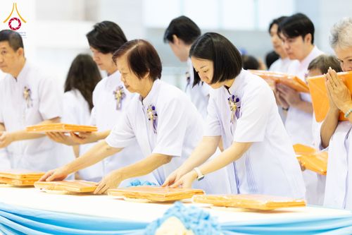 กลุ่มคนสวมชุดขาวกำลังวางผ้าไตรสีเหลืองทองบนโต๊ะในพิธีทางศาสนา