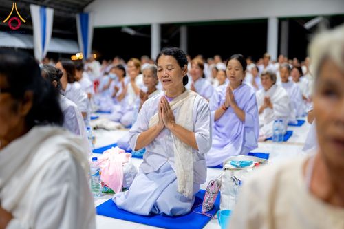 กลุ่มอุบาสิกาแก้วสวมชุดสีขาวนั่งพนมมือปฏิบัติธรรมอย่างสงบในอาคารปฏิบัติธรรม