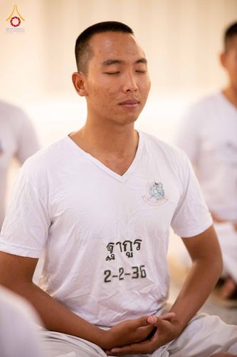 ชายหนุ่มสวมเสื้อสีขาวนั่งหลับตาทำสมาธิในกิจกรรมปฏิบัติธรรม