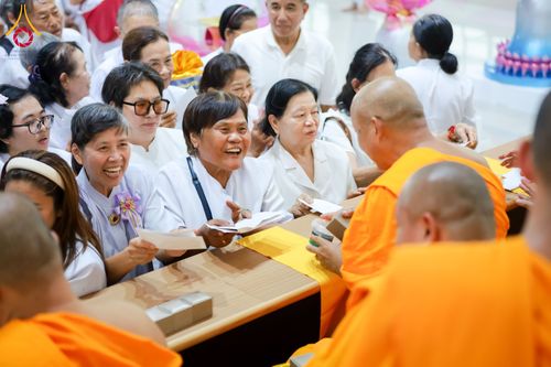 กลุ่มพุทธศาสนิกชนสวมชุดขาวกำลังถวายปัจจัยแด่พระภิกษุสงฆ์ด้วยความเลื่อมใสศรัทธาภายในงานบุญ