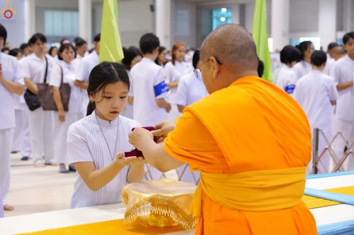 พระภิกษุกำลังมอบพระของขวัญให้เด็กหญิงในชุดสีขาวท่ามกลางผู้เข้าร่วมพิธี